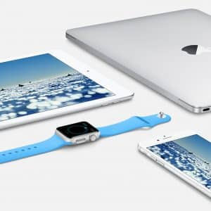 An assortment of Apple devices on a white surface including a silver MacBook, a silver iPad displaying a blue water scene, a silver iPhone showing the same water scene, and an Apple Watch with a blue band displaying a black screen, showcasing the seamless integration of the Apple ecosystem.