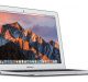 A silver MacBook Air laptop with its screen displaying a mountain landscape at sunset. The laptop is shown from a slight side angle, open and powered on, with the macOS desktop visible, including various app icons in the dock at the bottom. Exciting news: Apple plans to release a cheaper MacBook Air by the end of this year.