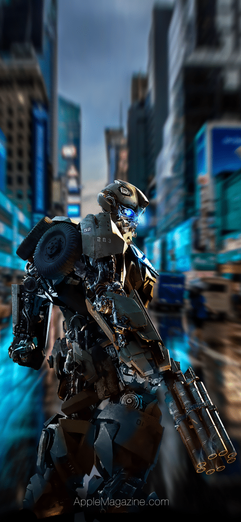 A detailed robot with blue LED lights on its eyes and components stands in a well-lit, futuristic city street filled with blurred motion effects. The robot appears to be made from various mechanical parts, including a tire on its shoulder and a multi-barreled arm cannon, perfect for an iPhone X wallpaper featured in AppleMagazine.