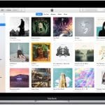 A MacBook displays the Apple Music app open on the Library tab, reminiscent of iTunes. Various album covers are visible, organized in a grid. The sidebar on the left shows options like Recently Added, Artists, Songs, Albums, and more. The top bar has controls for playback and navigation.