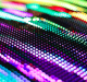 A close-up image of colorful, vibrant LED lights arranged in rows, creating a mesmerizing pattern with shades of green, purple, blue, and yellow. The slight blur gives an impression of movement and dynamic energy, reminiscent of the potential seen in future MicroLED displays from Apple.