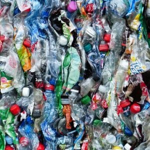 A close-up view of a compressed bale of various plastic waste materials including crushed bottles, wrappers, and caps of different colors and sizes. The chaotic yet intriguing pattern catches the eye, much like how scientists are captivated by a mutant enzyme that devours plastic.