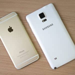 A gold Apple iPhone with the logo displayed on the back is placed next to a white Samsung smartphone, its logo visible. Both phones are resting on a wooden surface. The iPhone has a smooth metallic finish, while the Samsung phone features a textured back, like two contenders awaiting a jury decision.