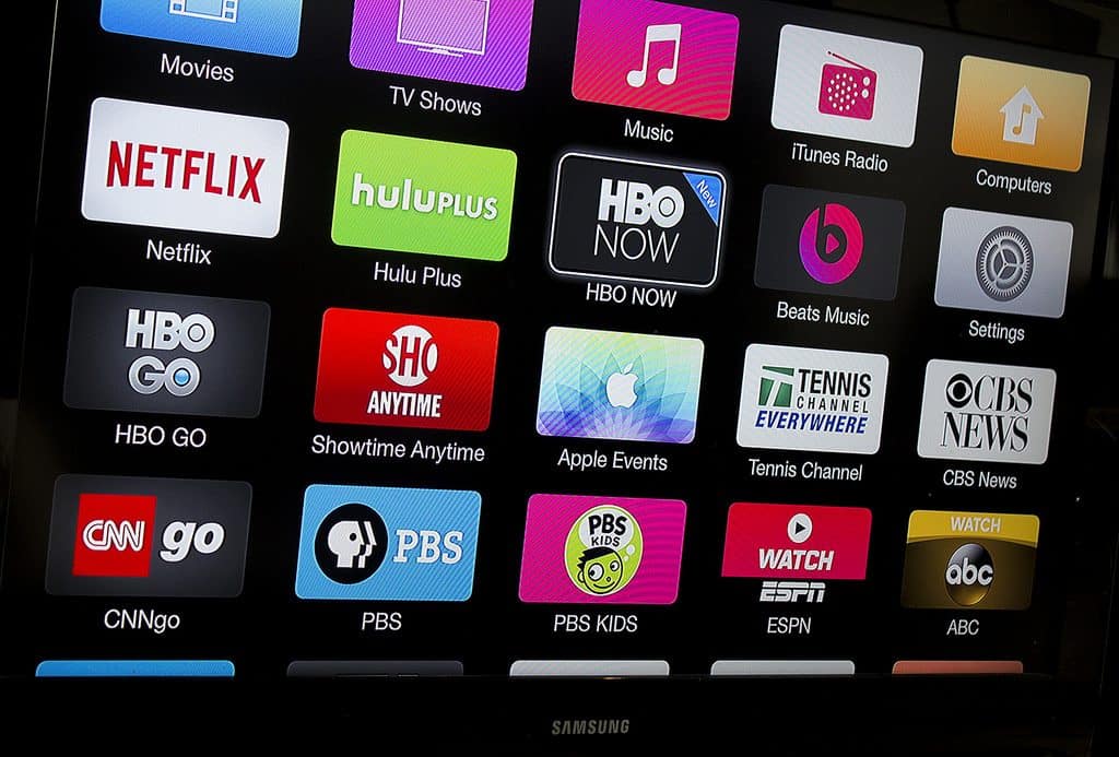 A TV screen displays a user interface with various app icons, including Netflix, Hulu Plus, HBO GO, Showtime Anytime, Apple TV app, Tennis Channel, CBS News, CNNgo, PBS, ESPN, and Watch ABC. The screen is part of a Samsung device optimized for your favorite streaming subscriptions.