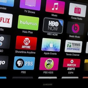 A TV screen displays a user interface with various app icons, including Netflix, Hulu Plus, HBO GO, Showtime Anytime, Apple TV app, Tennis Channel, CBS News, CNNgo, PBS, ESPN, and Watch ABC. The screen is part of a Samsung device optimized for your favorite streaming subscriptions.