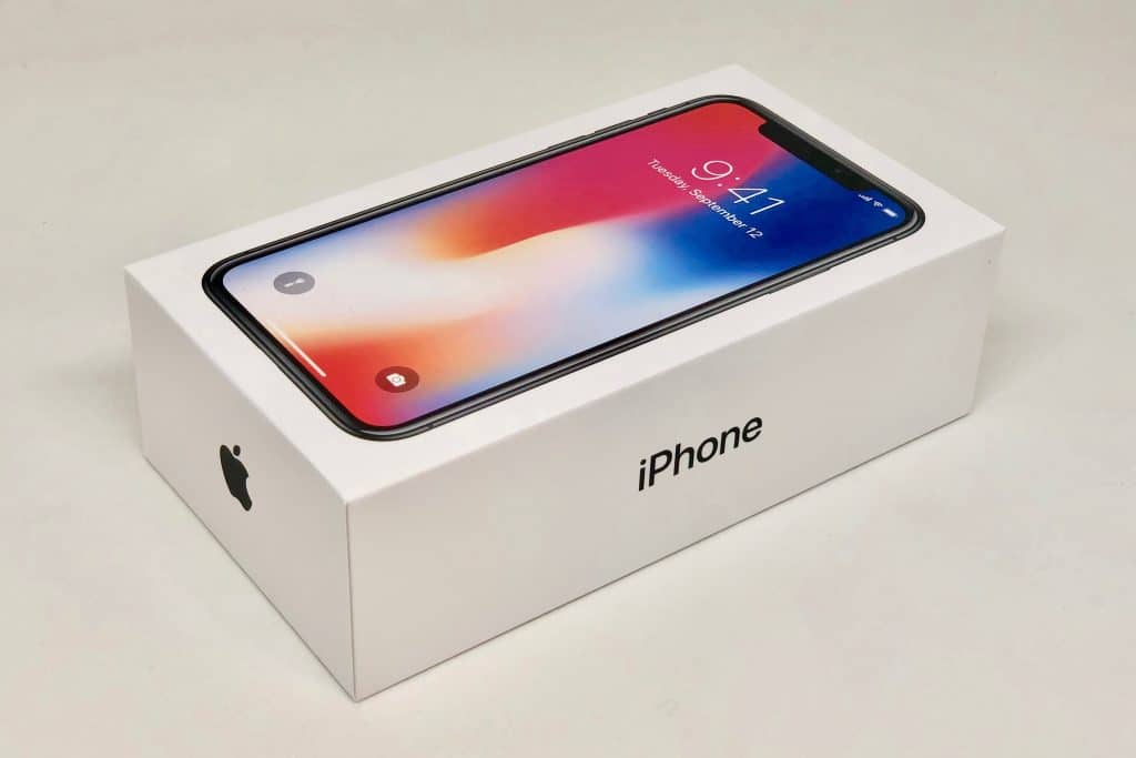 A white iPhone box with the word "iPhone" and the Apple logo on the side, containing an iPhone X with a display showing 9:41 AM and a colorful wallpaper. The box is set against a plain light background, showcasing one of the best displays of the year.