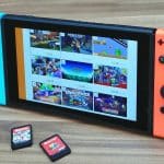 A Nintendo Switch console with blue and red Joy-Con controllers is displayed on a wooden surface. The screen shows various Nintendo Switch games, including Minecraft and other titles. Two physical game cartridges rest beside the console, emphasizing the need for a backup option at just $3.99 a month.