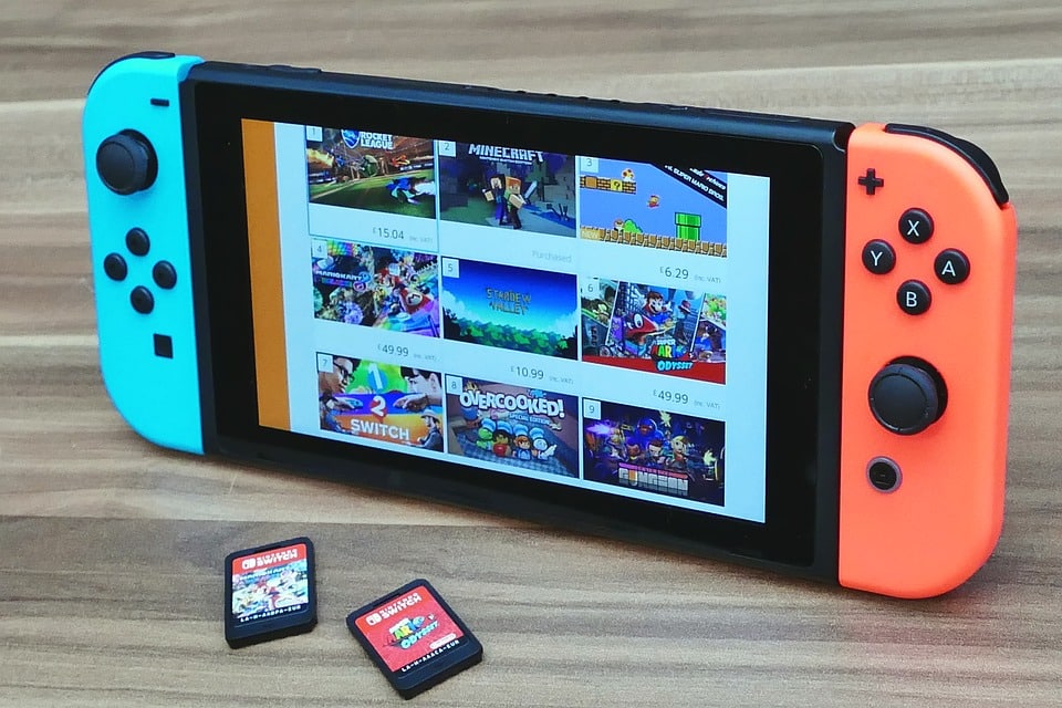 A Nintendo Switch console with blue and red Joy-Con controllers is displayed on a wooden surface. The screen shows various Nintendo Switch games, including Minecraft and other titles. Two physical game cartridges rest beside the console, emphasizing the need for a backup option at just $3.99 a month.