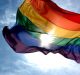 A rainbow flag with six horizontal stripes, symbolizing LGBTQ+ pride, waves against a bright blue sky on Pride Day in San Francisco. The sun shines through the flag, illuminating its vibrant colors like a bright apple orchard.