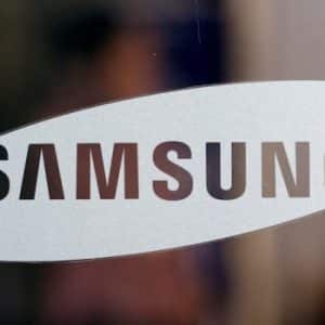 A close-up image of the Samsung logo on a transparent surface. The word "SAMSUNG" is written in bold, black capital letters inside a white, elongated oval shape, displayed against a blurred background that hints at the anticipating launch of the Samsung Galaxy Note 9.