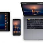 A MacBook, iPad, and iPhone are displayed side by side, each showing the same nighttime image of the Golden Gate Bridge. The MacBook screen is larger, showcasing photo editing software, while the iPad and iPhone display edited versions of the photo using the Photos app.