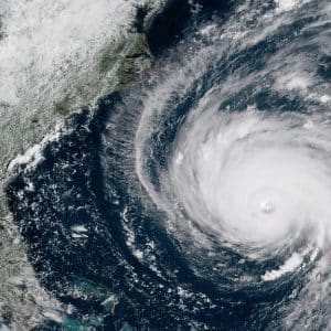 A satellite image shows Hurricane Florence, a powerful storm with a well-defined eye, approaching the southeastern coast of the United States. The large, spiraling storm covers a substantial portion of the Atlantic Ocean, with the green coastline of the U.S. visible on the left.