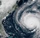 A satellite image shows Hurricane Florence, a powerful storm with a well-defined eye, approaching the southeastern coast of the United States. The large, spiraling storm covers a substantial portion of the Atlantic Ocean, with the green coastline of the U.S. visible on the left.