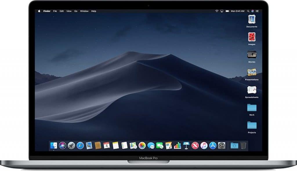 An open MacBook Pro displaying its home screen with a Mojave desert sand dune wallpaper. Various application icons such as Finder, Safari, Siri, and others are visible in the dock at the bottom of the screen. The menu bar at the top shows system menus as Apple launches MacOS Mojave.