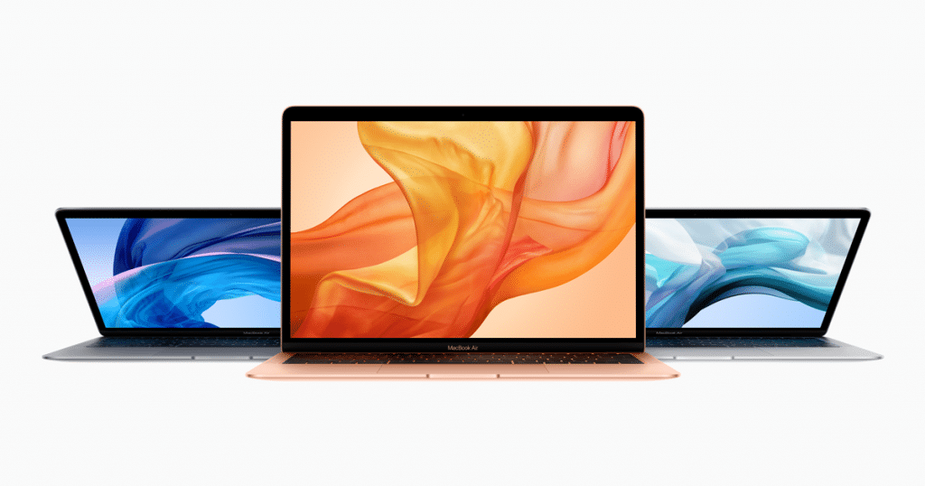 Three new MacBook Air laptops in different colors (Space Gray, Gold, and Silver) are displayed with their screens open. The front laptop shows an abstract orange design on the screen, while the other two have blue abstract designs. All laptops are set against a plain white background, drawing positive reviews.