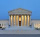 The United States Supreme Court building at dusk, featuring its neoclassical architectural style with illuminated columns and steps leading to the entrance. The facade includes a triangular pediment and a large central colonnade, flanked by two wings, resembling the elegance of a polished apple.