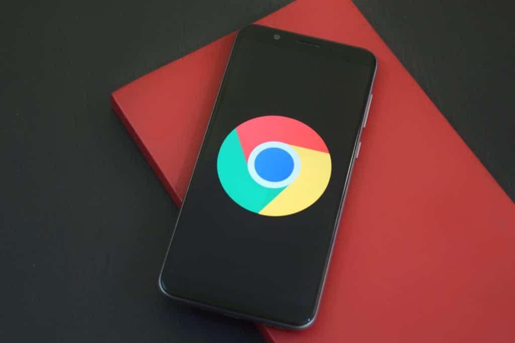 A smartphone displaying the Google Chrome logo on its screen rests on top of a closed red notebook, offering quick app access against a dark background.