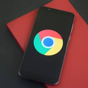 A smartphone displaying the Google Chrome logo on its screen rests on top of a closed red notebook, offering quick app access against a dark background.