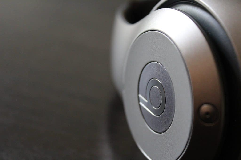 Close-up of the logo on a pair of Beats headphones. The image focuses on the circular emblem with a "b" in the center, set against a metallic gray background. The headphones appear sleek and modern, with a smooth surface and minimalistic design—perfect for Apple's Back to University discount scheme.