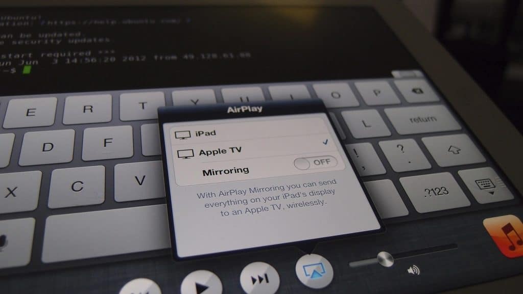 An iPad screen showing a pop-up menu for AirPlay, including options like Apple TV and LG devices, with a toggle for Mirroring set to off. The background reveals a keyboard and terminal window filled with coding text, seamlessly integrating tech into your HomeKit ecosystem.