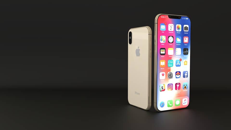 A gold-colored iPhone XS with an Apple logo is displayed against a black background. The phone's screen shows a variety of app icons, including settings, calendar, and social media apps, and is positioned upright next to the back of another identical phone.