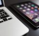 A close-up image of a laptop keyboard on the left side and a tablet with a home screen displaying various app icons on the right side, reflecting Apple's 2019 plans. Both devices are placed on a dark surface.