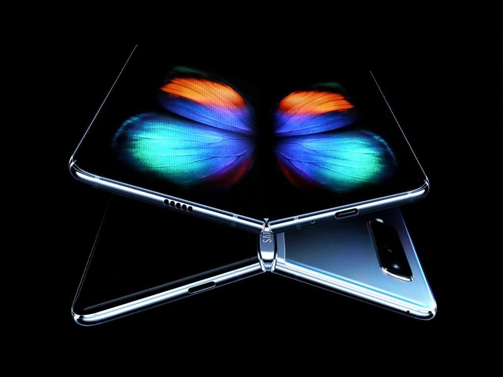 A futuristic $2,000 Samsung foldable smartphone is shown partially open in a dark environment. The screen displays a vibrant, colorful butterfly graphic. The back of the phone is sleek and metallic with a dual-camera setup.