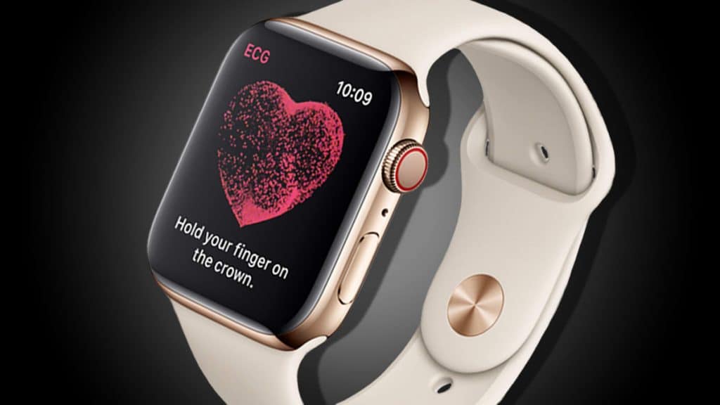 An Apple Watch with a light-colored band is displaying an ECG feature on its screen, including a heart graphic with the text "Hold your finger on the crown." The watch case is gold with a red ring around the digital crown. The time shown is 10:09.