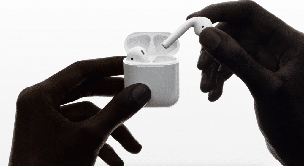 Two hands hold a pair of white wireless earbuds, with one hand holding the charging case and the other removing an earbud. The background is a plain, light gradient. Experience the sleek design and enhanced sound quality highlighted in our New AirPods 2 review.