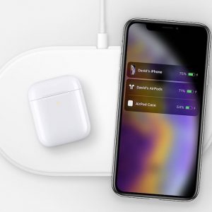 An Apple AirPower wireless charging pad holds a white AirPods case and a smartphone. The smartphone screen displays a charging interface showing "David's iPhone" at 75%, "David's AirPods" at 71%, and "AirPod Case" at 54%.