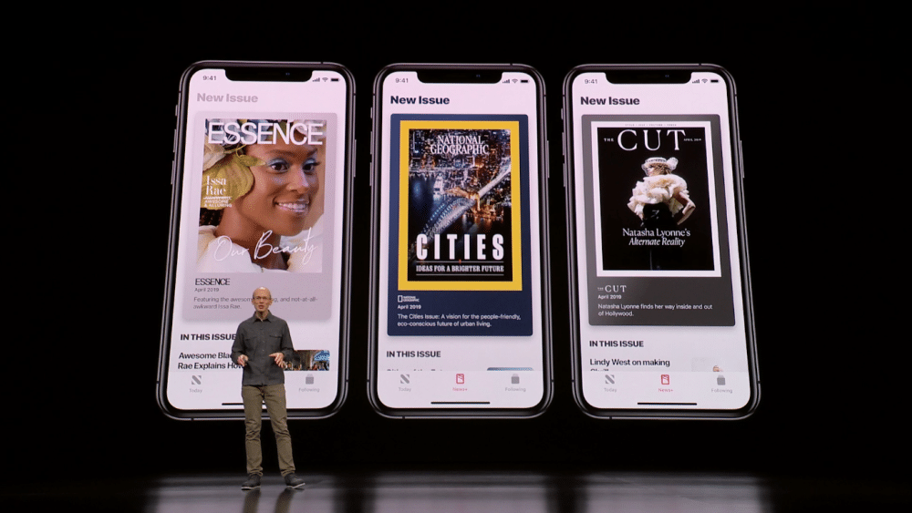 A person stands on stage in front of a large screen displaying three smartphones. Each phone shows the cover of a different magazine: "ESSENCE," "CITIES," and "CUT." The heading above each phone reads "New Issue" via Apple News+ for just $9.99/mo.