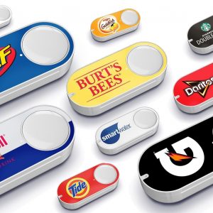 Several Amazon Dash Buttons are displayed, each branded with different logos, including Nerf, Goldfish, Burt's Bees, Starbucks Doubleshot, RedBull, Smartwater, Doritos, Tide, and Gatorade. The buttons are white with a large logo on each—a nostalgic reminder as Amazon discontinues the Dash Button line.