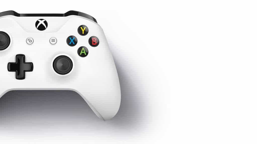 A white Xbox One S gaming controller with black joysticks and buttons is displayed against a white background. The buttons are colorful: yellow Y, blue X, green A, and red B. There is a black directional pad on the left and Microsoft brand markings on the top center.