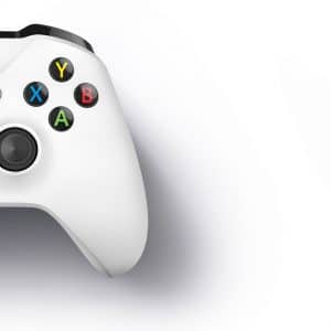 A white Xbox One S gaming controller with black joysticks and buttons is displayed against a white background. The buttons are colorful: yellow Y, blue X, green A, and red B. There is a black directional pad on the left and Microsoft brand markings on the top center.