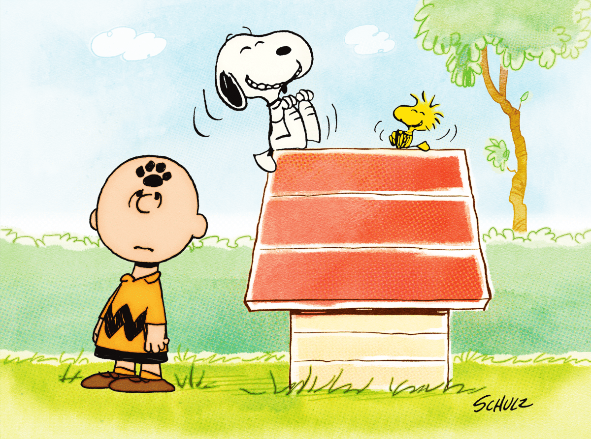 Charlie Brown stands next to Snoopy, who is joyfully dancing on top of his red doghouse, with Woodstock perched beside him. The background features green bushes, a tree, and a blue sky. The scene is lively and colorful, capturing the playful essence of the Peanuts in Space episode on Apple TV.