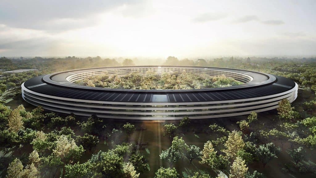 Aerial view of a large, modern, circular building surrounded by lush greenery and bathed in sunlight streaming through clouds overhead. This key priority structure, with its black-roofed concentric levels, appears seamlessly integrated into the forested environment.