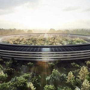 Aerial view of a large, modern, circular building surrounded by lush greenery and bathed in sunlight streaming through clouds overhead. This key priority structure, with its black-roofed concentric levels, appears seamlessly integrated into the forested environment.