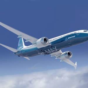 An airplane with blue and white livery marked "Boeing 737 MAX" ascends in a clear blue sky with a few clouds below. The aircraft, featuring automated systems and two engines mounted under its wings, boasts a sleek, modern design.