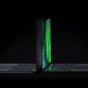 Two sleek, black laptops—resembling the new MacBook Pro models launched in 2021—are open and positioned back-to-back against a dark background. Their screens display vivid green imagery, and the minimalist keyboards are visible. The lighting accentuates their futuristic and elegant appearance.