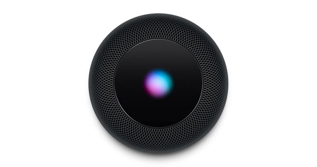 An overhead view of a black cylindrical HomePod with a glowing, multicolored touch control panel on top. The mesh exterior is textured and the light on the panel displays a blend of pink, blue, and green hues. This sleek Apple device offers premium sound quality at an attractive price.