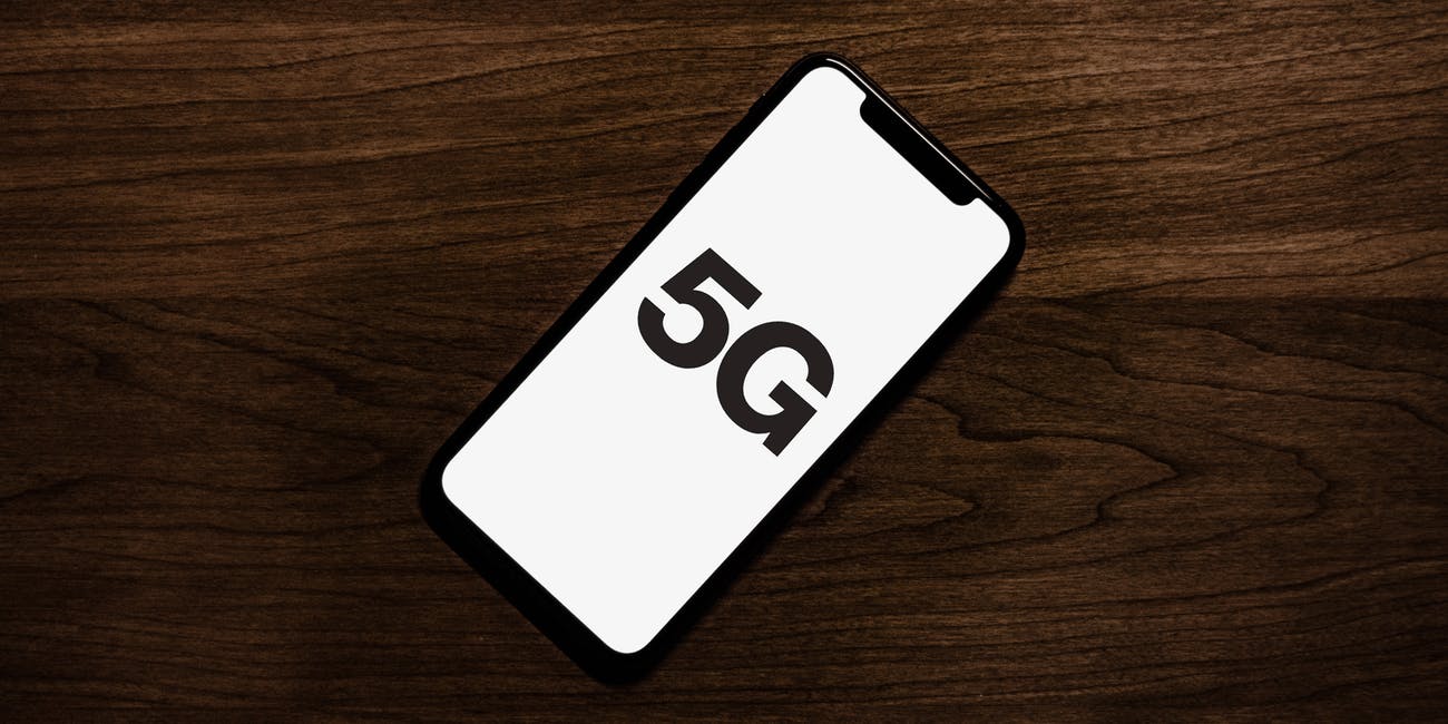 A sleek smartphone with a black frame lies on a dark wooden surface, displaying the text "5G" on its screen. This could be one of Apple’s 2020 5G iPhone models, part of the 200 million units shipped globally.