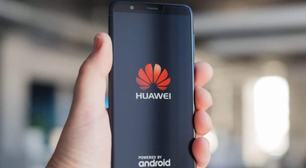 A hand holding a smartphone displaying the Huawei logo and the words "HUAWEI" and "Powered by Android," showcasing its resilience amidst Chinese sanctions, on a blurred background.