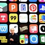 A person stands on stage in front of a large screen displaying a grid of various app icons, including popular apps like Pinterest, PlayStation, Lego, Hue, and others. The individual is wearing glasses and a black long-sleeve shirt while discussing how to top up your account using Apple ID.