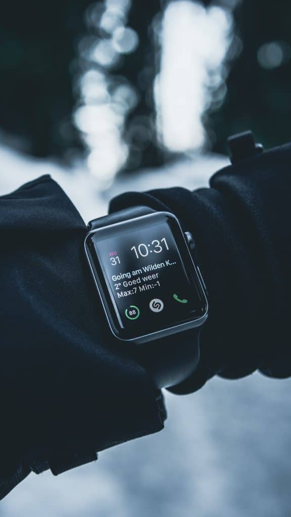 A person wearing a black glove and an Apple Watch, displaying the time as 10:31 and a message about the weather, with a snowy outdoor background in soft focus. The smartwatch, awarded Display of the Year by a prestigious body, has several apps open, including phone and music apps.