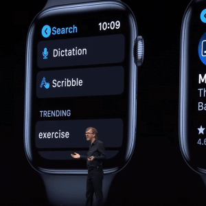 A person stands on a stage presenting Apple Watch features powered by watchOS 6. Three large Apple Watch screens are shown: one displaying the App Store with the Nike Run Club app, another showing search and trending options, and the third featuring the MLB At Bat app with ratings and age information.