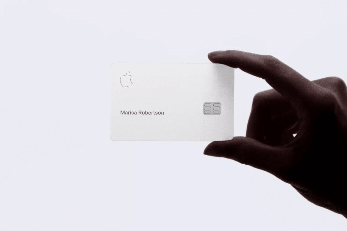 A hand holding an Apple Card is showcased. The card, issued by Goldman Sachs, is white with a minimalist design, featuring the Apple logo, cardholder's name "Marisa Robertson," and a chip on the right side. The background is white.