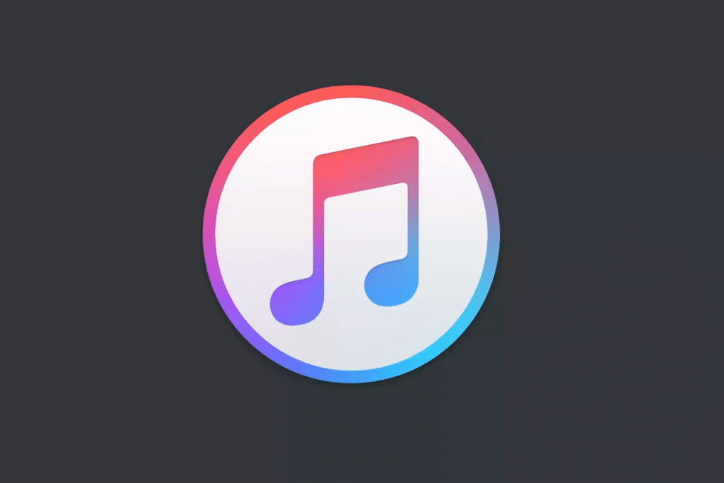 The image shows the iTunes branding logo, featuring a white music note on a circular gradient background that transitions from pink at the top to blue at the bottom. The logo is set against a dark gray background, embodying Apple's sleek design aesthetic.