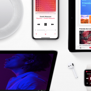 A flat lay of Apple devices including an iPad, iPhone, Apple Watch, MacBook, HomePod, and a pair of AirPods. The iPad and iPhone display music apps while the Apple Watch shows a "Now Playing" screen. This scene highlights the connected Apple ecosystem and its seamless access to Apple Music's 60 million paying subscribers.