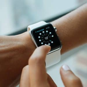 Close-up of a person’s wrist wearing an Apple Watch with a white band and a weather app displayed on the screen. The screen shows "Montreal," the temperature as 19°C, and weather icons. The person's other hand is pointing at the screen, reflecting an increase in shipments for this popular gadget.