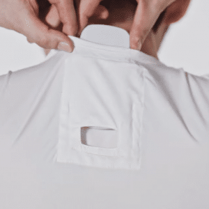 A person wearing a white shirt is adjusting a small, flat white device attached to the back of their neck. The device, part of Sony's personal air conditioning system, is tucked into a pocket with a square cut-out on the shirt's neck area, showcasing a modern design against a plain white background.